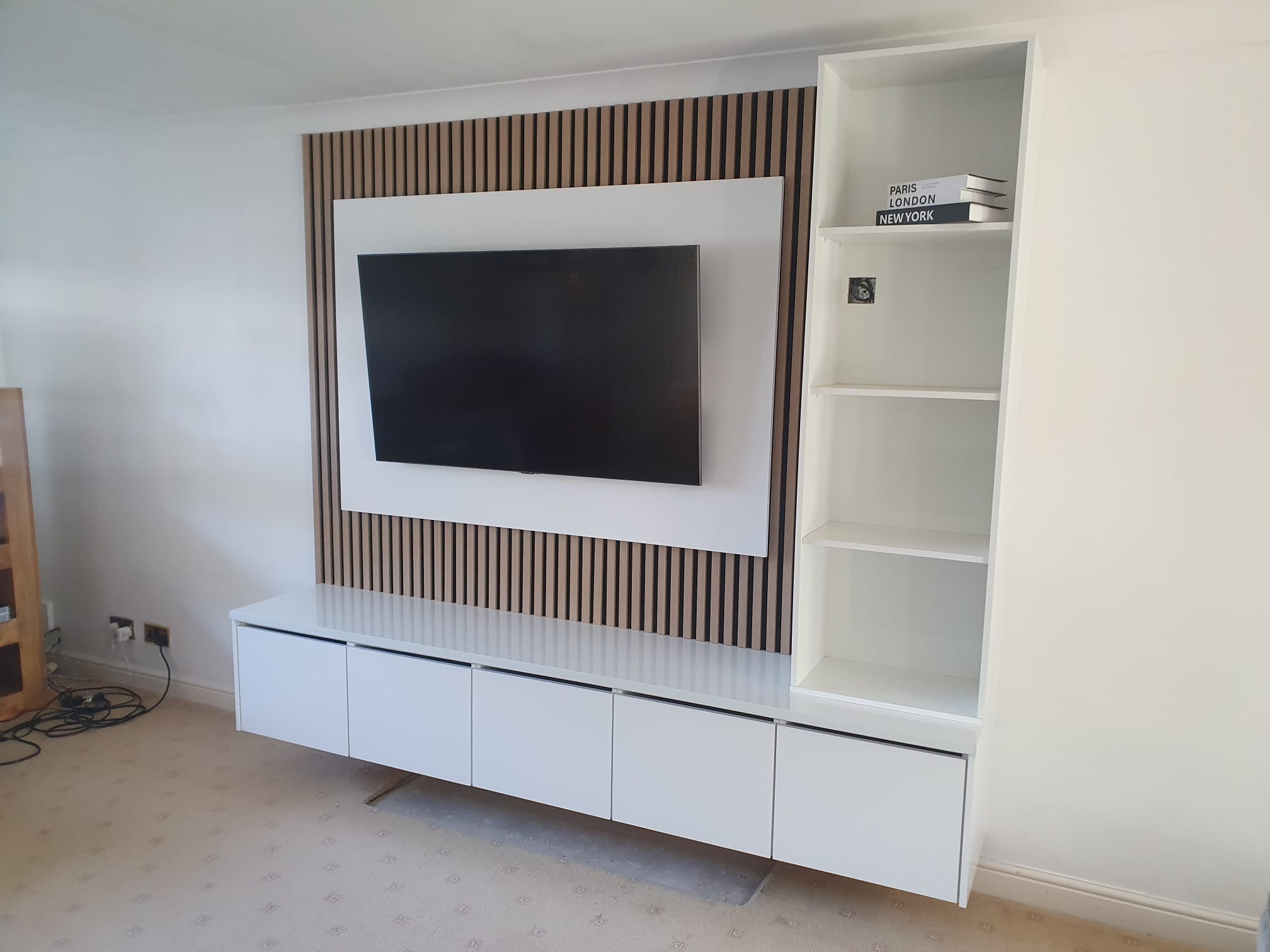 Media wall with oak slat panelling and floating cabinets, angled view